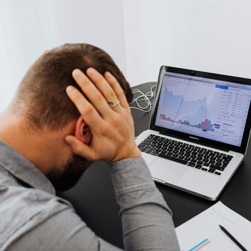 man with laptop on desk terrified by stock market chart
