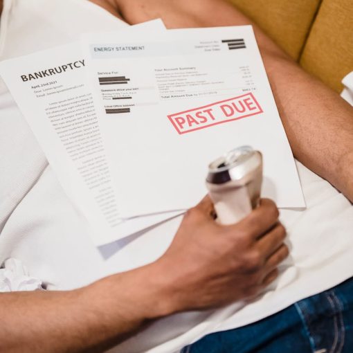 man lying down under unpaid bills holding a can