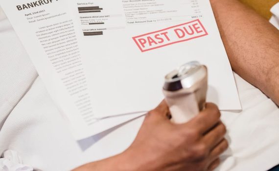 man lying down under unpaid bills holding a can