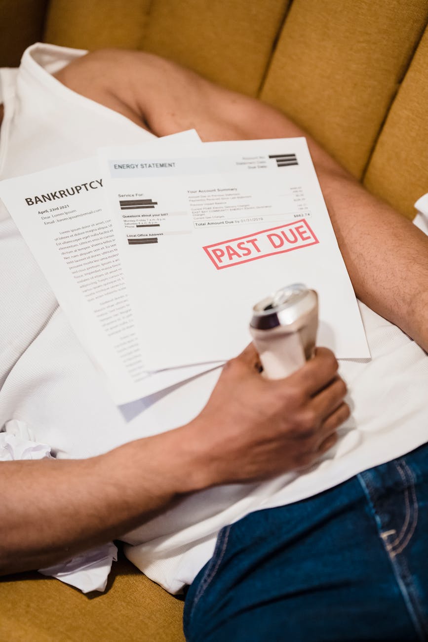 man lying down under unpaid bills holding a can