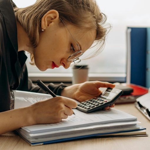 a woman writing on a book while holding a calculator