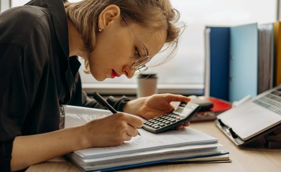a woman writing on a book while holding a calculator
