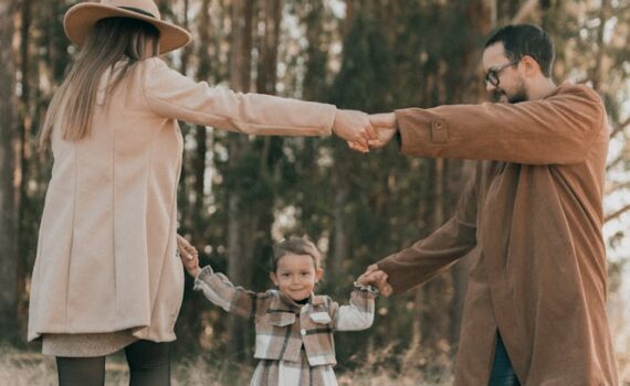 a family with a little daughter dancing in a forest in autumn